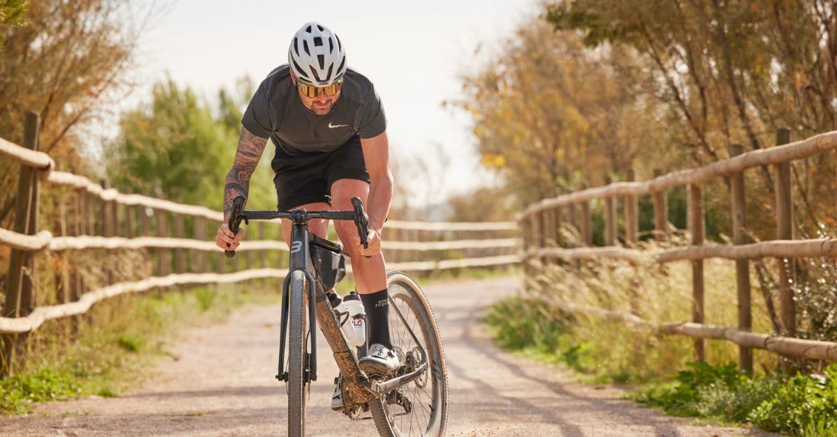 Focused cyclist riding on a gravel path, flanked by rustic fences and autumnal trees.